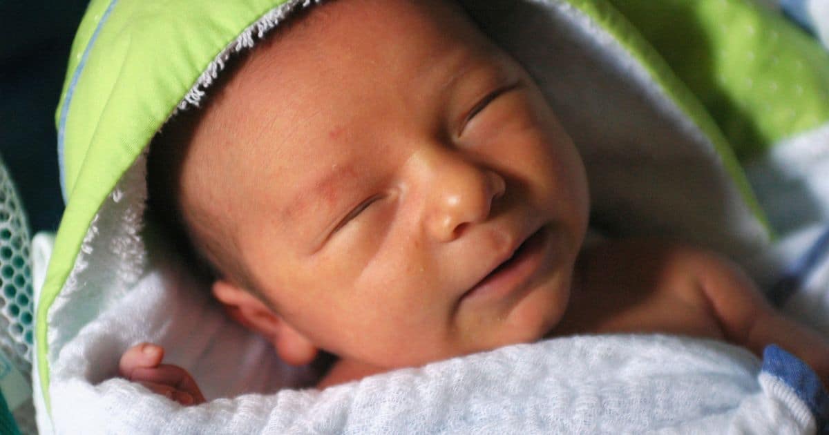 newborn baby with eyes closed wrapped in green towel after a bath