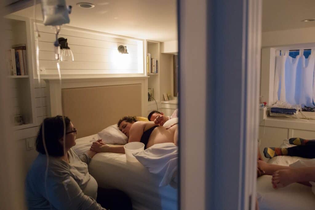 Sharon Muza, birth doula, quietly holding hands with a resting laboring person during a home birth